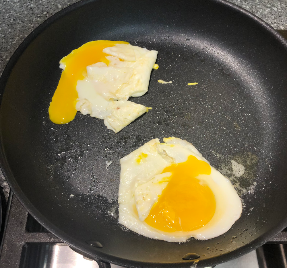 Two eggs with broken yolks frying in a nonstick pan.