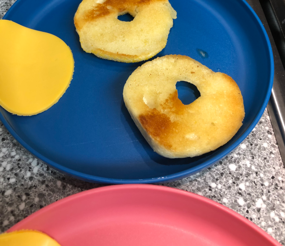Bagel halves are now shown on a small blue plate, with toasty light brown patches on them. A circle of cheese is draped on the left edge of the blue plate.