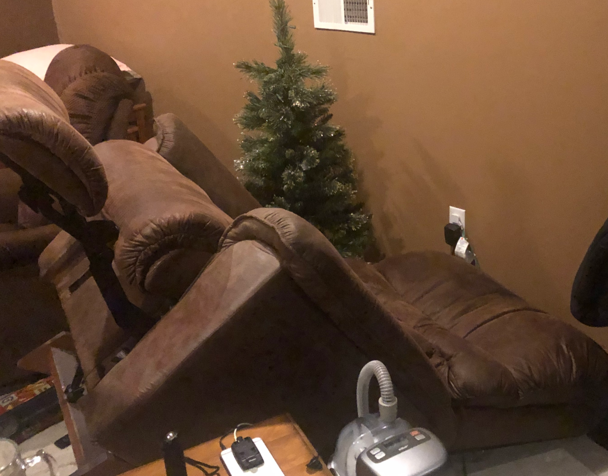 A brown faux-suede recliner is seen reclined, but also tipped onto its back. The headrest is against a wall to the right, and also against the floor. The footrest extends up to the left at a 50 to 60 degree angle.